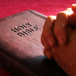 His word the holy bible. Hands folded in prayer on closed Bible.
