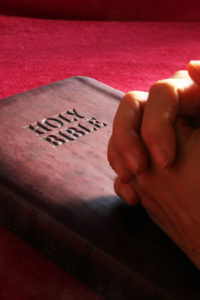  His word the holy bible. Hands folded in prayer on closed Bible.